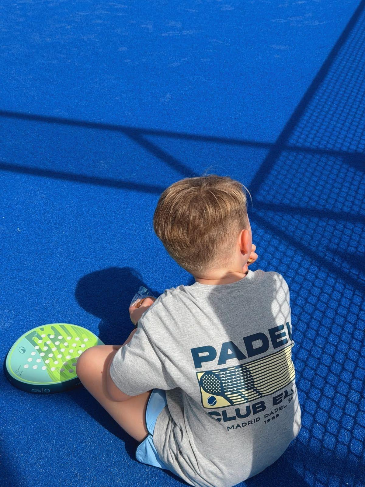 Jeune joueur assis sur une piste de padel, raquette posée à côté de lui