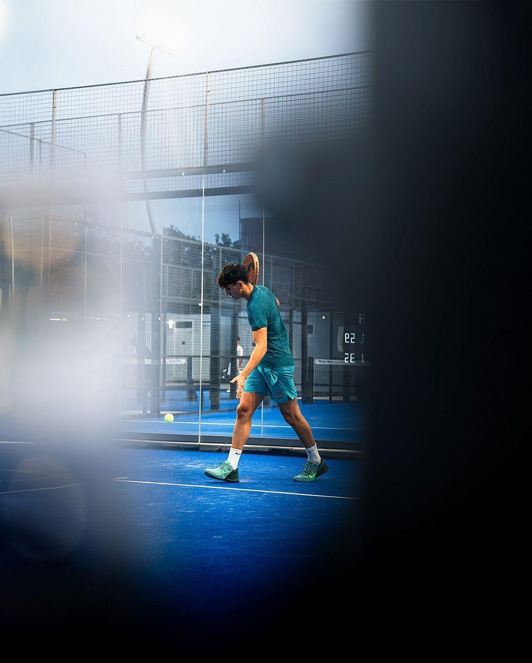 Piste de padel vue à travers une vitre, joueur flou au fond