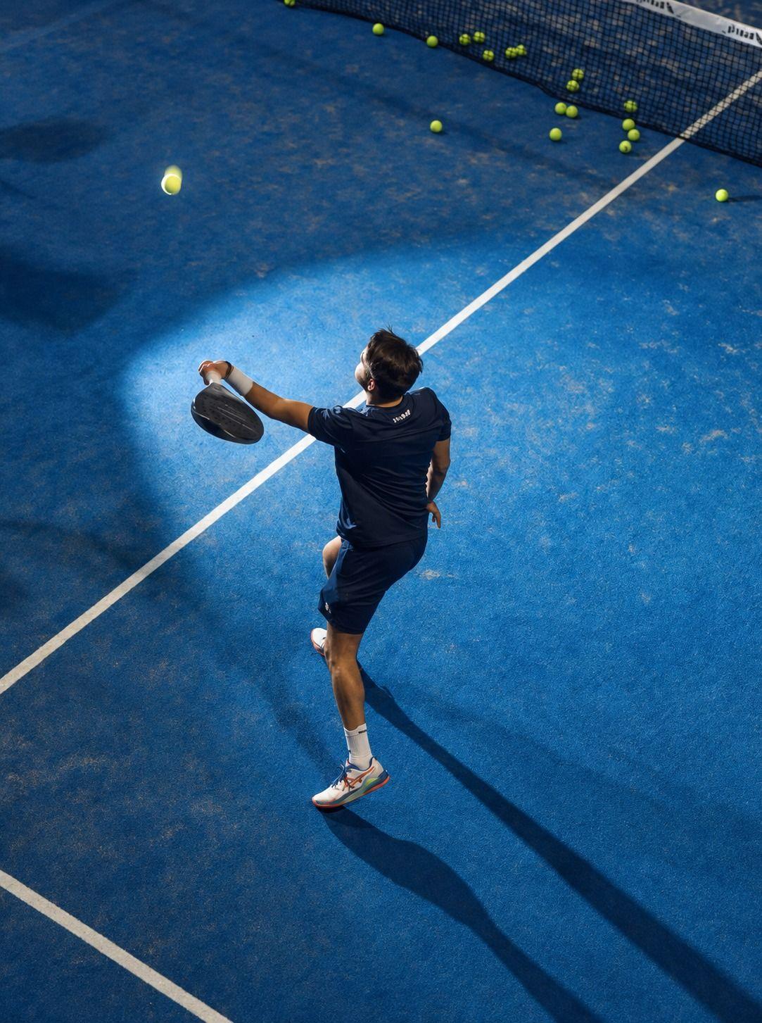Joueur de padel vu d’en haut, en pleine frappe sur une piste bleue éclairée