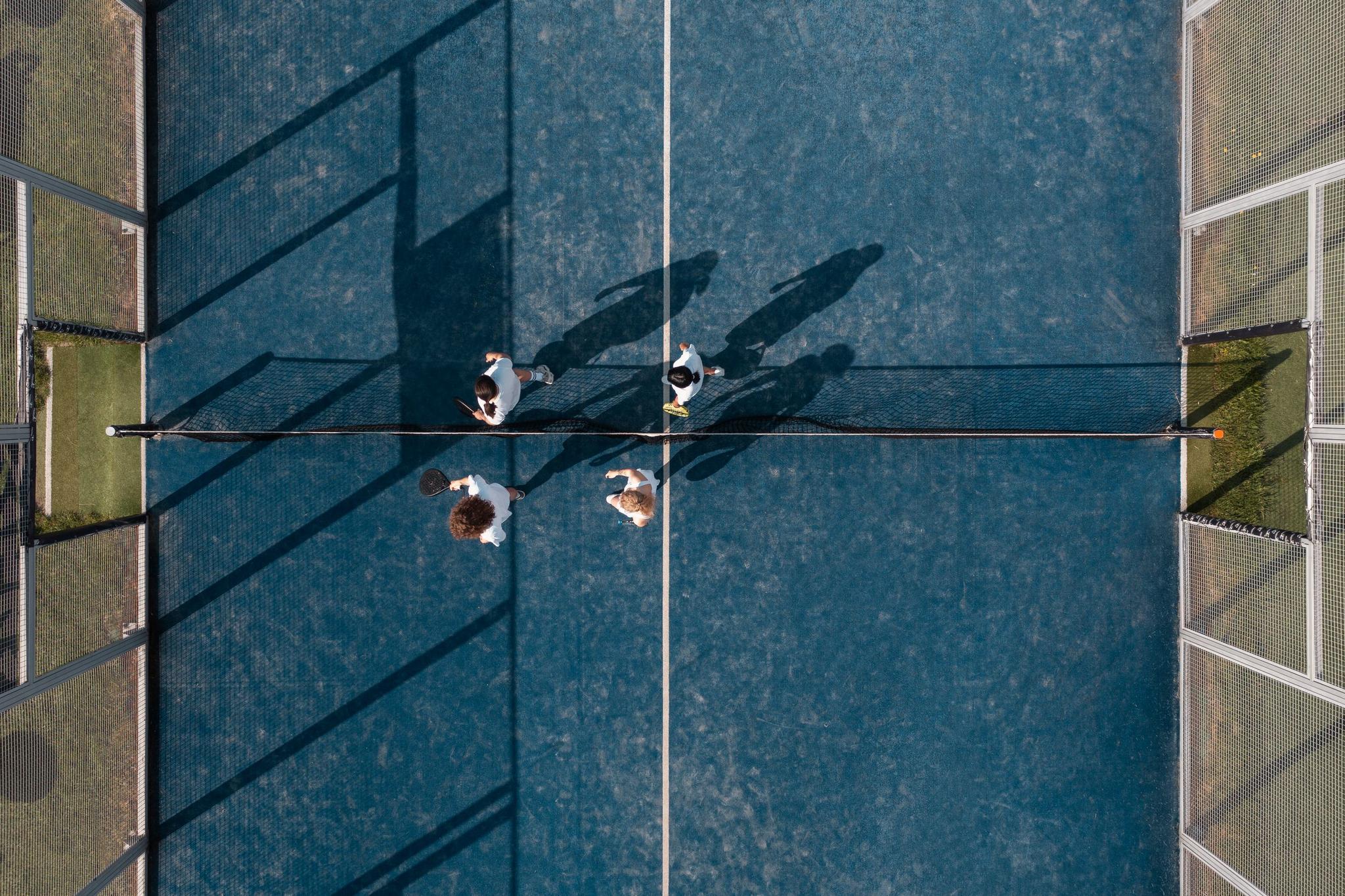 Match de padel vu du dessus, quatre joueurs sur une piste bleue
